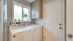 A laundry room with two Whirlpool washers, a window with a plant, and a white door. - Cozy Roseburg Home w/ Deck + Gas Grill! (Roseburg)