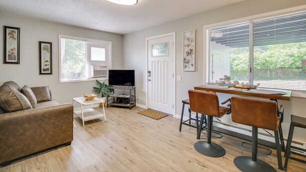 A modern living room with a sofa, TV, dining table, and chairs. - Cozy Roseburg Home w/ Deck + Gas Grill! (Roseburg)
