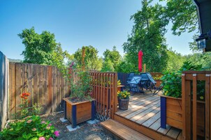 Una terraza de madera con mobiliario exterior, rodeada por una valla de madera y diversas plantas.