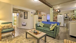 A cozy living room with a green patterned sofa, a wooden coffee table, and a kitchen area with a refrigerator and microwave. - Cozy & Vintage Cedar City Apartment w/ Fire Pit! (Cedar City)