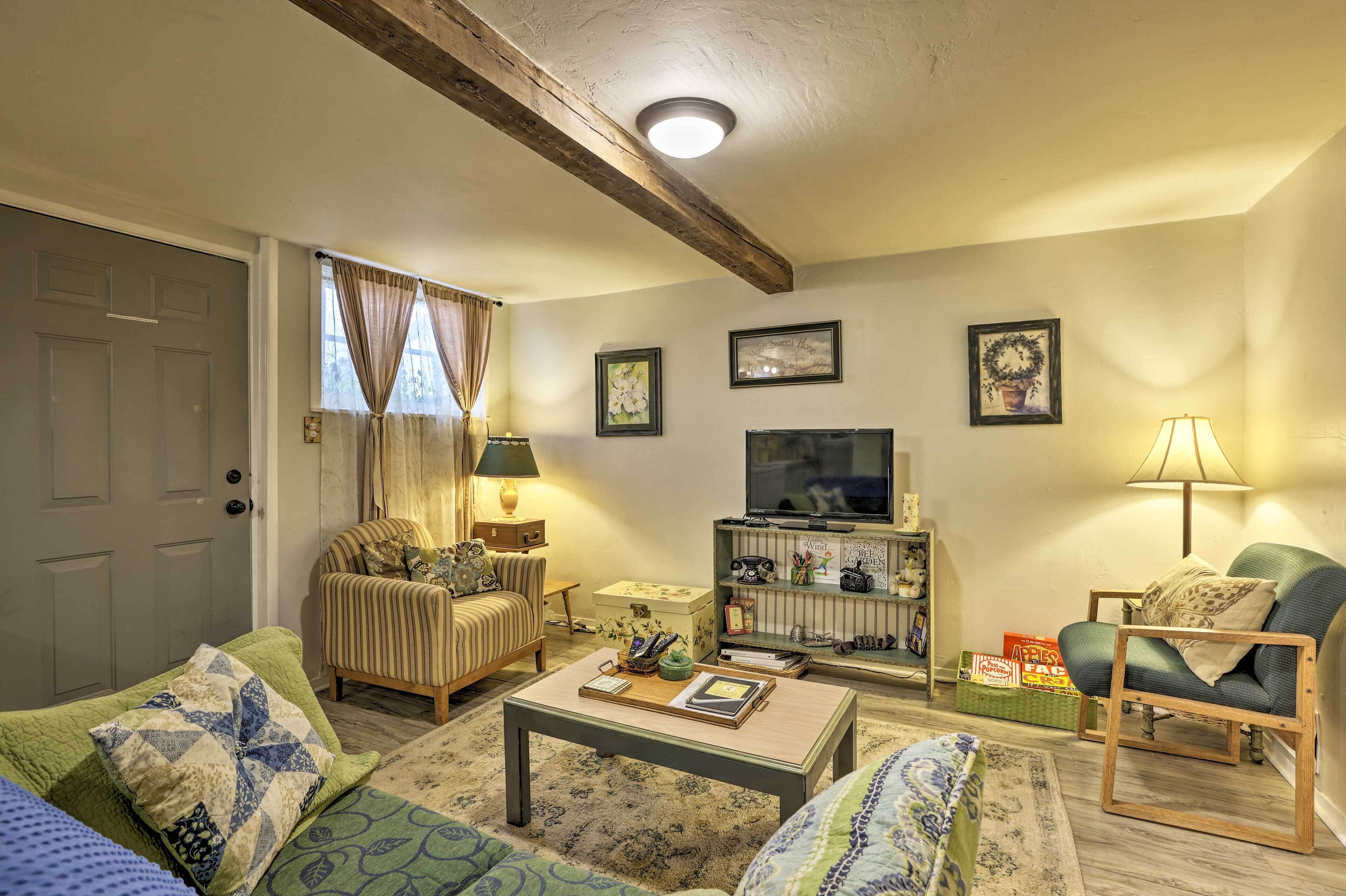 Una sala de estar acogedora con un sofá, un sillón, una mesita de centro y un televisor. Se aprecia una estantería con objetos decorativos y una lámpara.