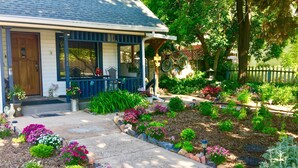 A house with a porch, a garden with various plants and flowers, and a bicycle leaning against the fence. - Cozy & Vintage Cedar City Apartment w/ Fire Pit! (Cedar City)