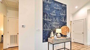 A hallway with a wooden floor, a wall with a sailboat pattern, a table with a lamp and decorative items, and a door. - 4 Mi to Boat Ramp: Charming Rockport Home (Rockport)