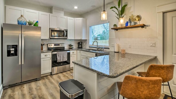 A modern kitchen with white cabinets, stainless steel appliances, granite countertops, and a central island with two chairs. - 4 Mi to Boat Ramp: Charming Rockport Home (Rockport)