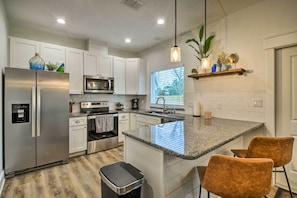 A modern kitchen with white cabinets, stainless steel appliances, granite countertops, and a central island with two chairs. - 4 Mi to Boat Ramp: Charming Rockport Home (Rockport)