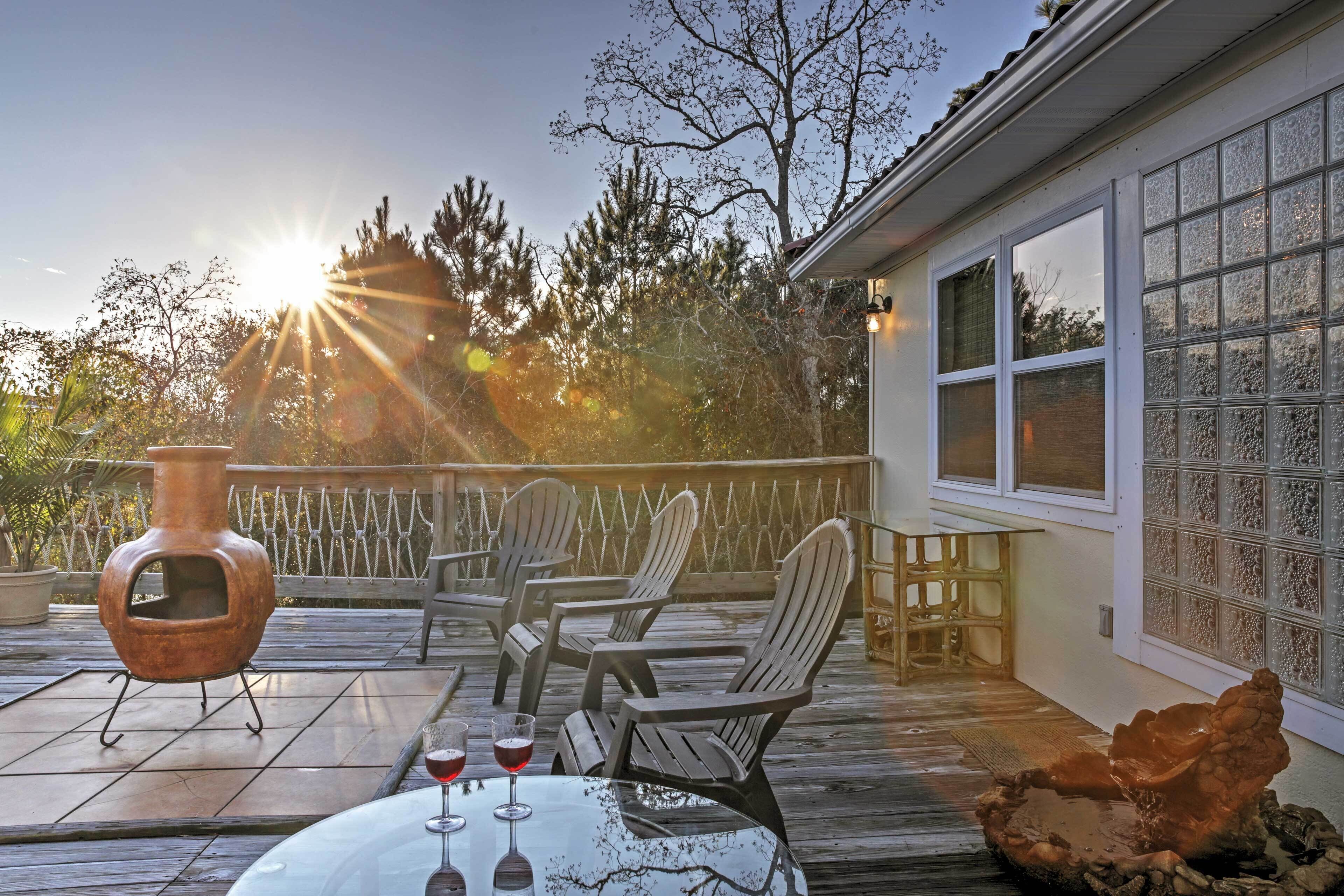 A wooden deck with chairs and a table, a rustic vase, and a glass of red wine.