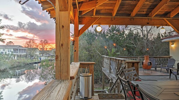 A wooden deck with a view of a lake, a metal trash can, and outdoor furniture. - Bay St. Louis House w/ Boat Dock & Launch! (Bay St Louis)