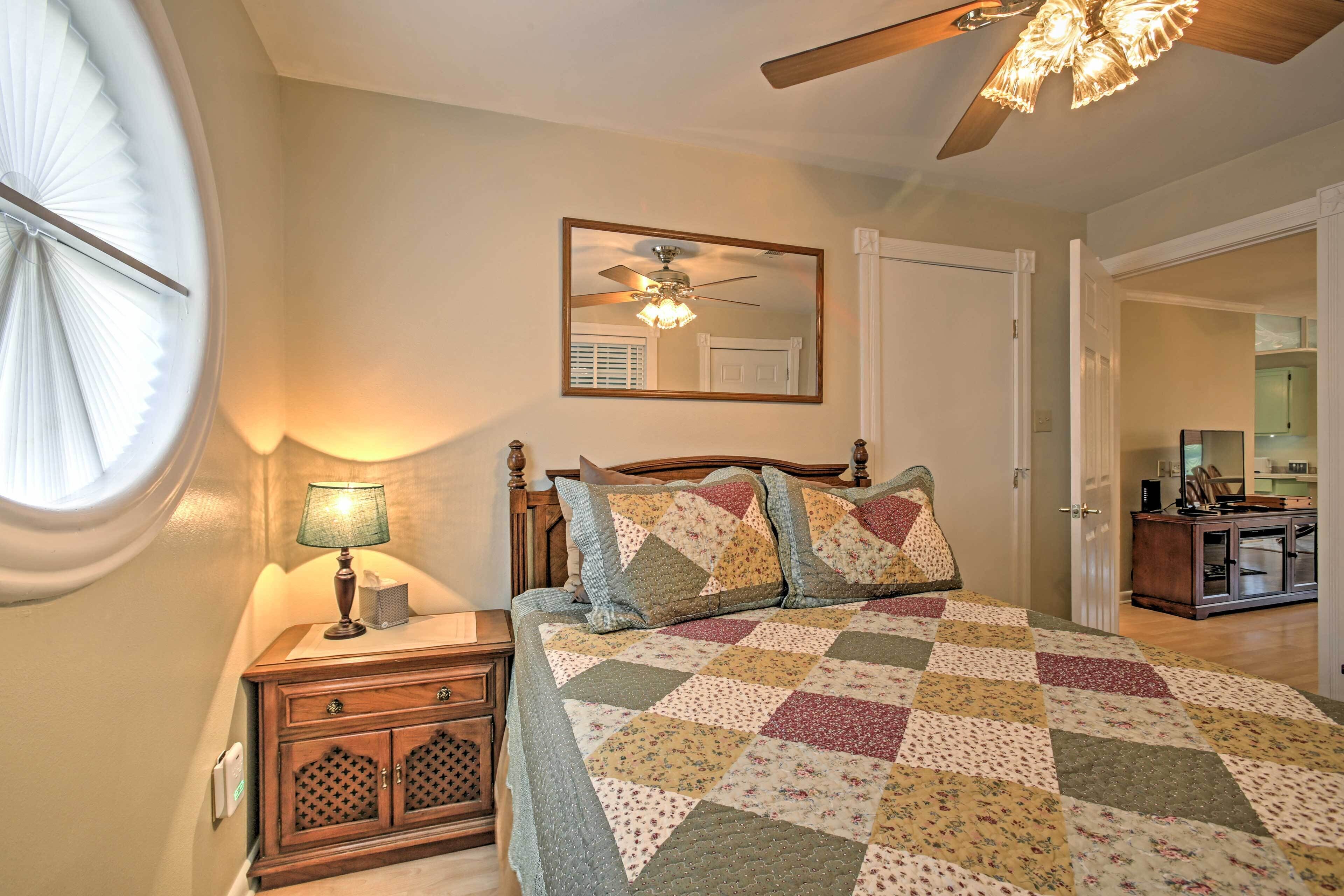 A bedroom with a wooden bed, a nightstand with a lamp, a ceiling fan, and a large mirror on the wall.