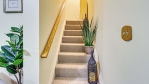 A staircase with a wooden handrail, beige carpeted steps, a potted plant, and a decorative vase.