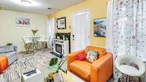 A living room with a sofa, a dining table with chairs, a fireplace, and a kitchen area.
