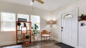 Une pièce comprenant un lit, une chaise en bois, une bibliothèque, une plante en pot, une lampe et une porte.