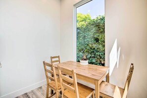 Un coin repas avec une table et des chaises en bois, une plante en pot et une vue sur la verdure par une fenêtre.