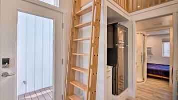 A modern interior with a wooden ladder leading to a balcony, a walk-in closet, and a bedroom with a bed and a window.
