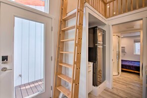 Un interior moderno con una escalera de madera hacia un balcón, un vestidor y un dormitorio con cama y ventana.