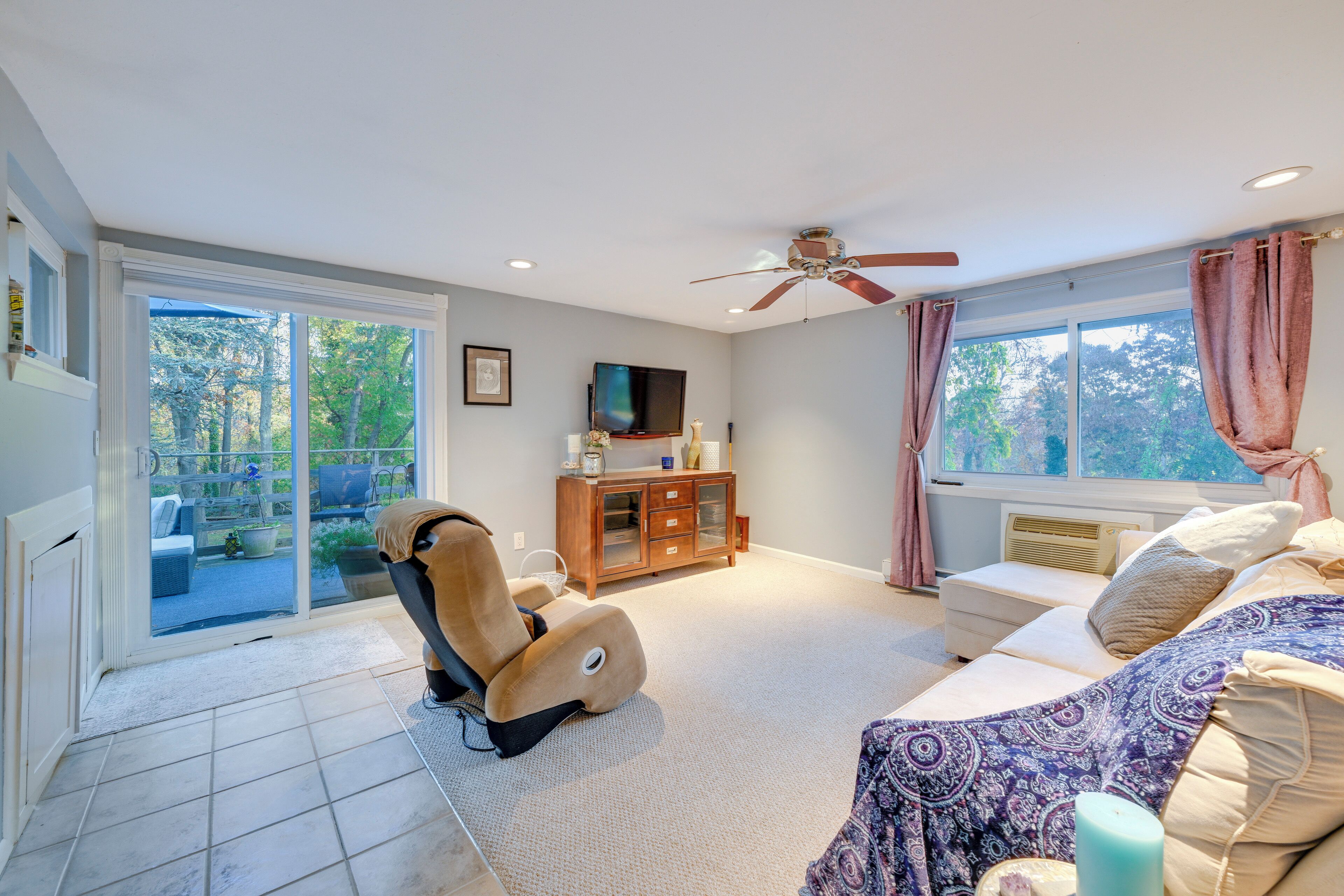 A spacious living room with a ceiling fan, a sofa, a recliner, a TV, and a sliding glass door leading to an outdoor area.