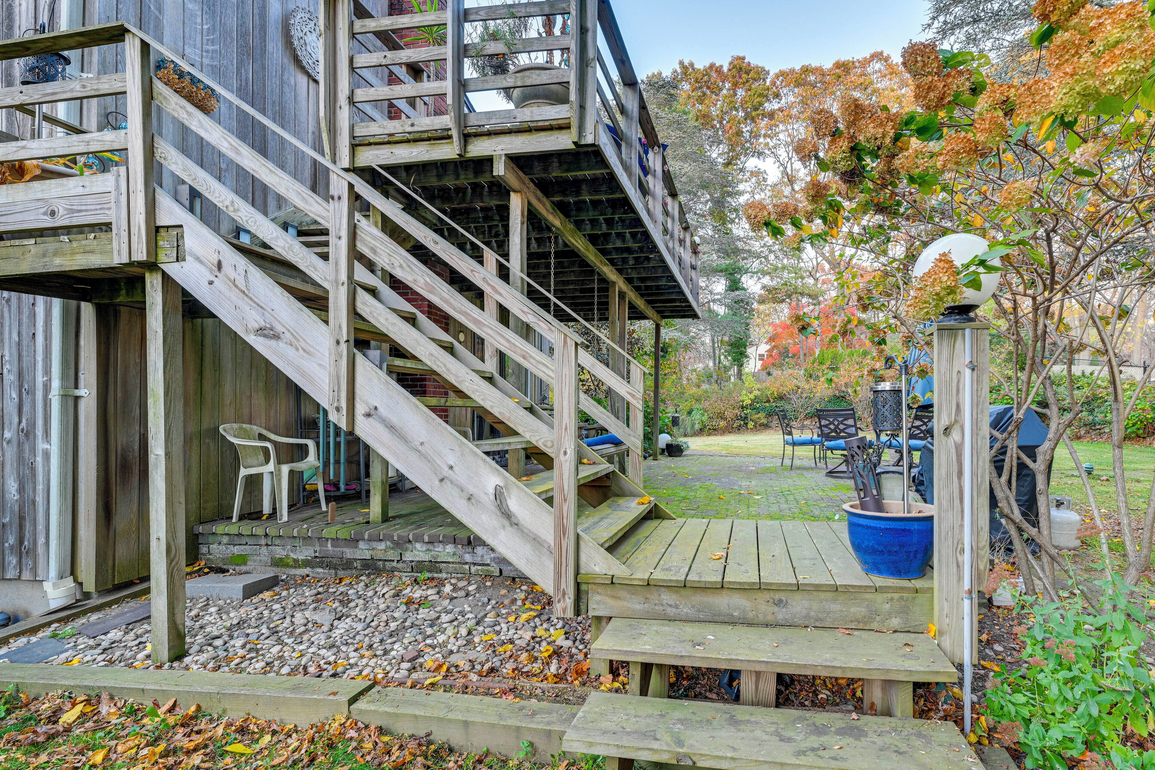 Une terrasse en bois avec un escalier menant à une zone abritée, le tout entouré d’un feuillage automnal.