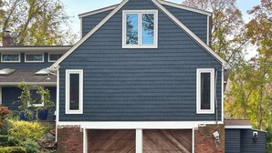 Ein zweistöckiges Haus mit dunkelgrauem Anstrich, weißer Verkleidung und einer Garage mit Holztüren.