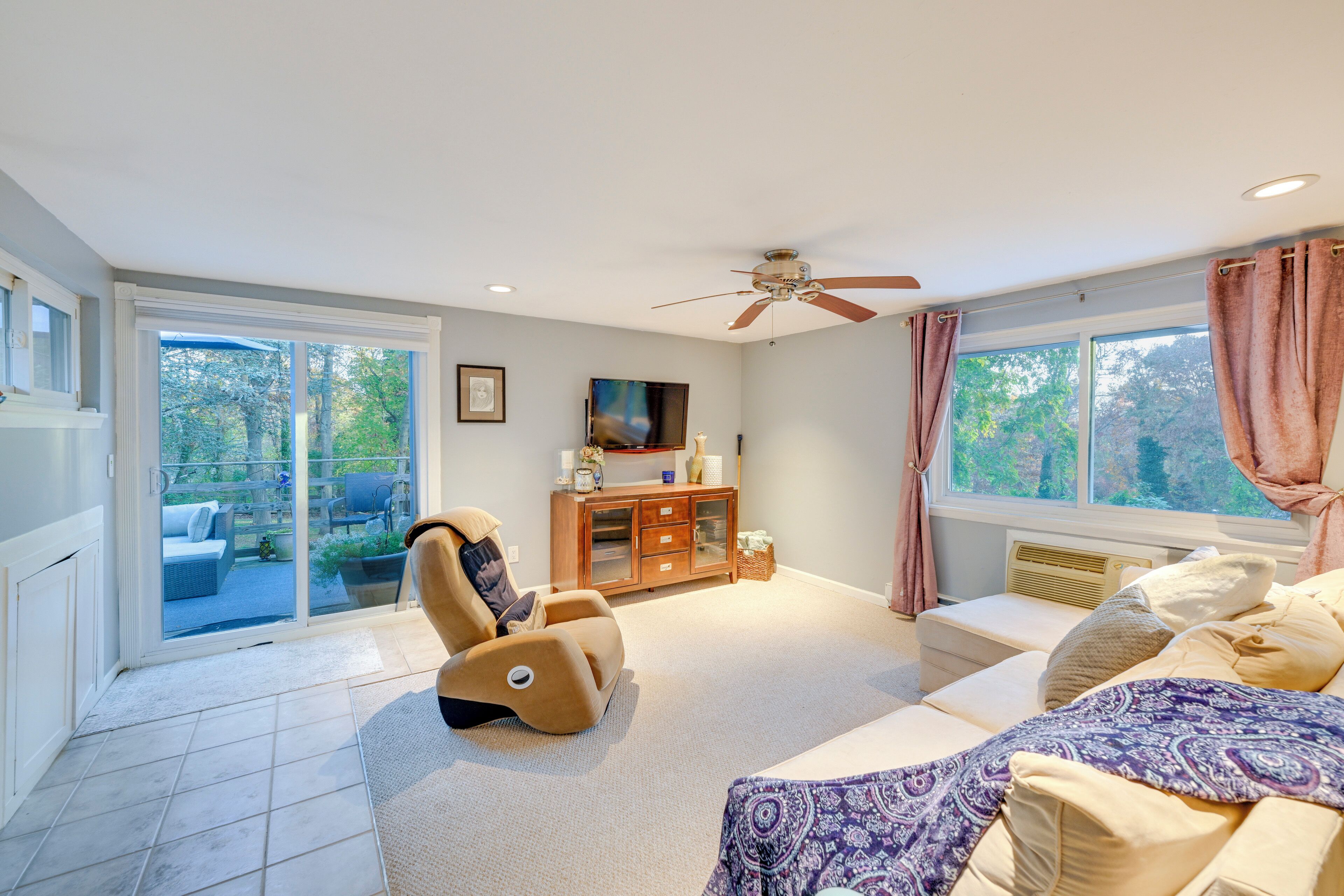 A spacious living room with a ceiling fan, a sofa, a recliner, and a TV on a wooden cabinet.