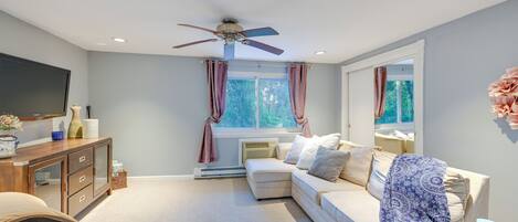 A living room with a sofa, a TV, a ceiling fan, and a window with curtains.