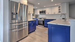 A modern kitchen with stainless steel appliances, white and blue cabinetry, and a central island. - Long Island Home Near Beaches & Golf (Bellmore)