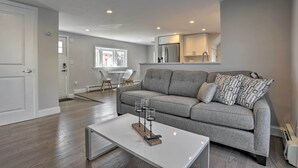 A modern living room with a grey sofa, a white coffee table, and a dining area with a white table and chairs. - Long Island Home Near Beaches & Golf (Bellmore)