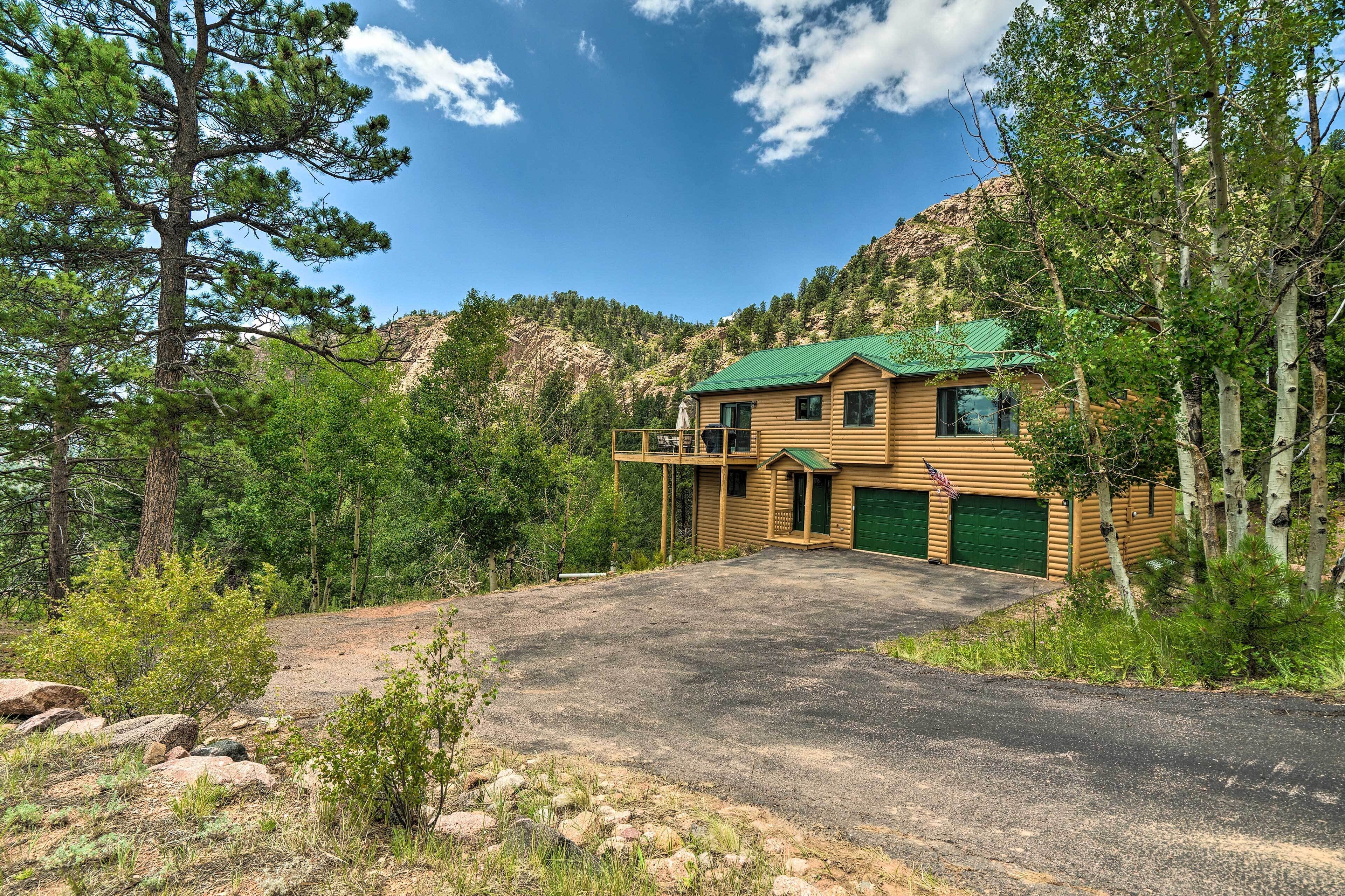 A log cabin with a green roof, a covered porch, and a garage.