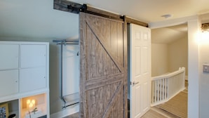 A room with a white door, a wooden sliding barn door, a white railing, and a shelf with candles. - Coastal Comfort & Golfers' Paradise in Sheboygan! (Sheboygan)