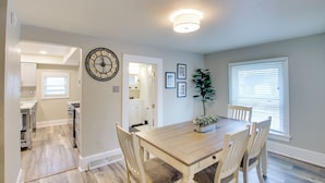 A dining area with a wooden table, four chairs, a clock, and framed pictures on the wall. - Coastal Comfort & Golfers' Paradise in Sheboygan! (Sheboygan)