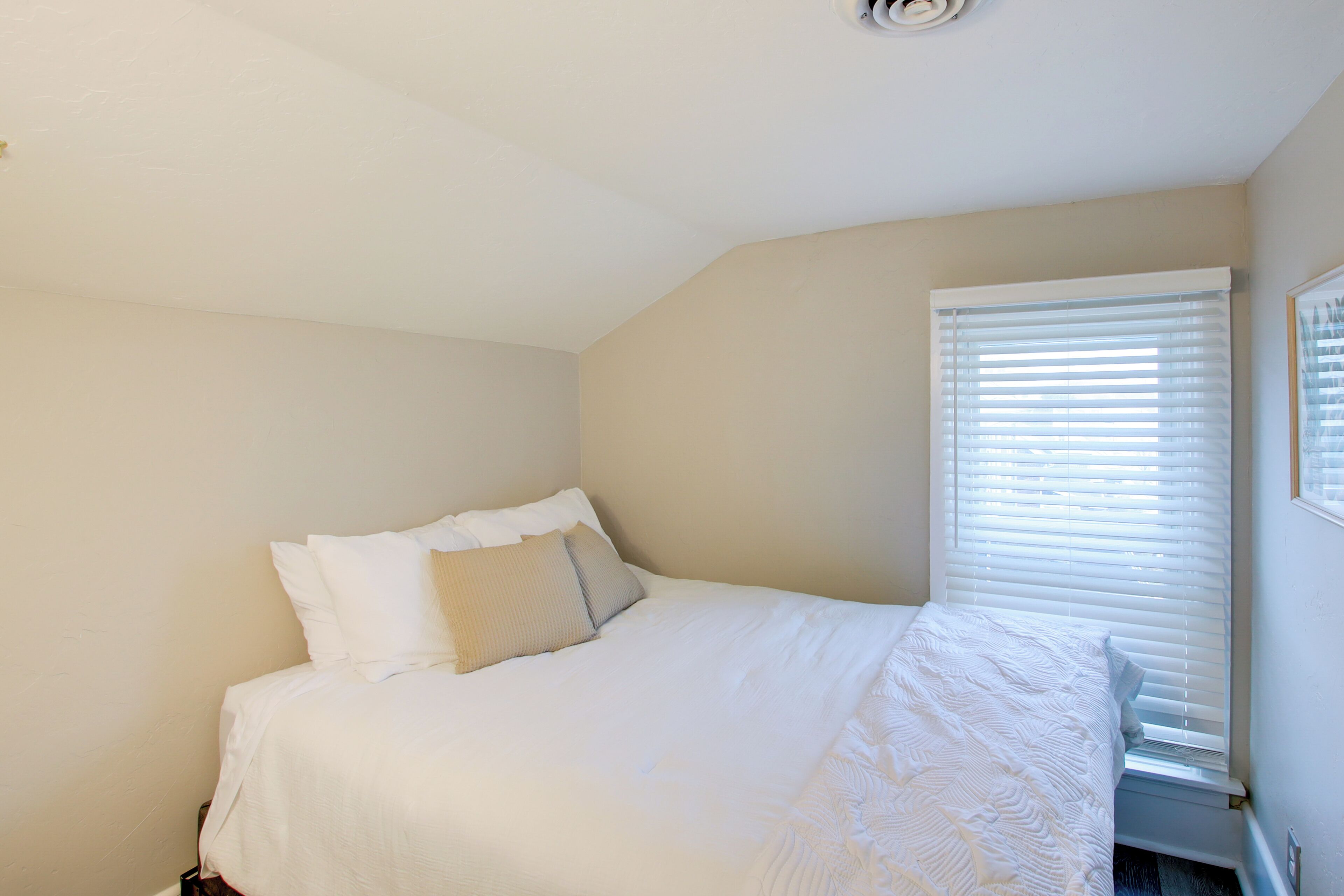 A bedroom with a bed, white bedding, a window with blinds, and a ceiling light.