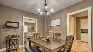 A dining area with a wooden table, four chairs, a chandelier, and a small shelf with glassware. - Chic & Cozy Greensboro Home, 2 Mi to Dtwn! (Greensboro)