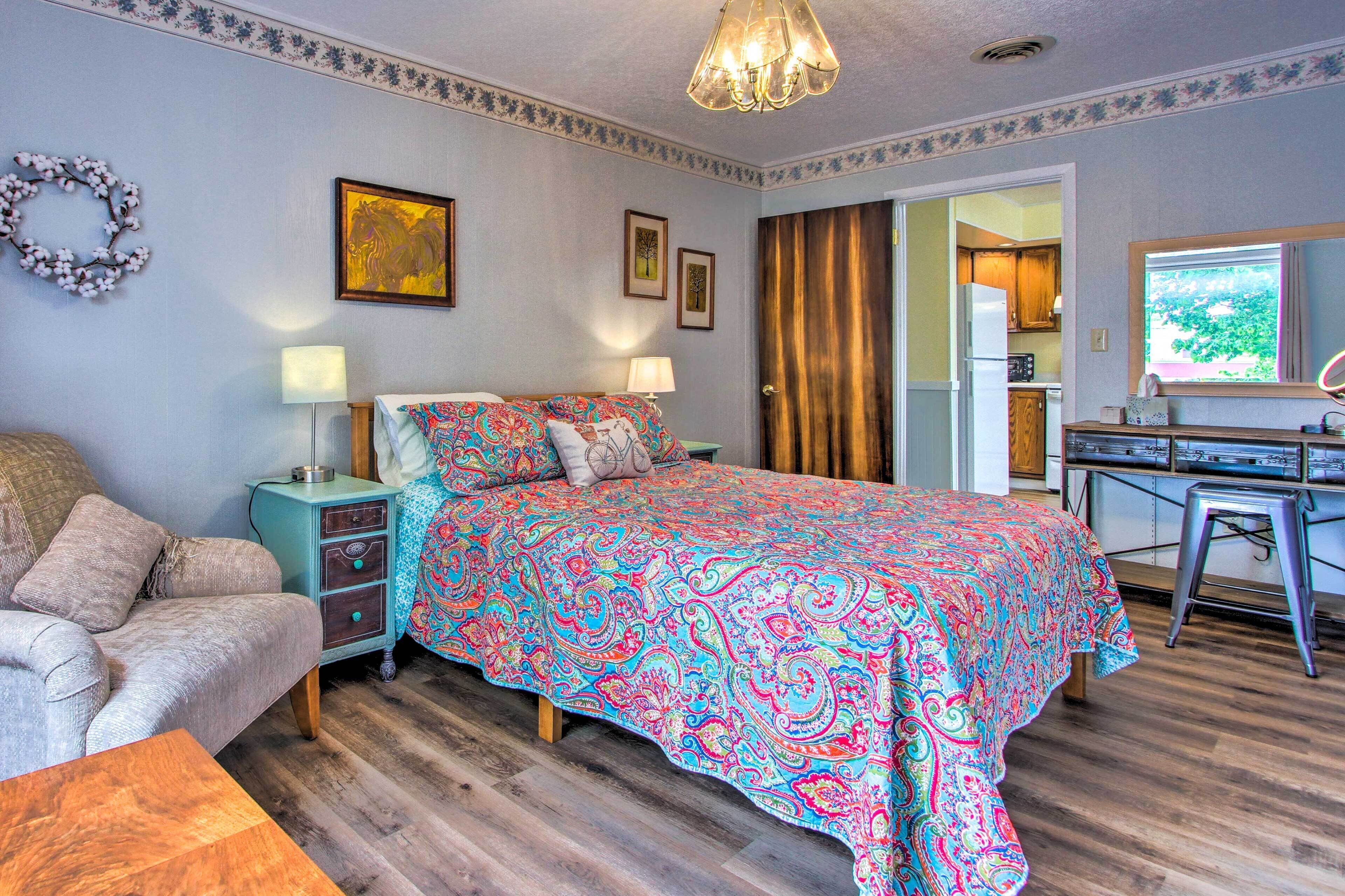 Quarto com cama, mesas de cabeceira, cômoda e vista para a cozinha.
