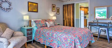 Quarto com cama, mesas de cabeceira, cômoda e vista para a cozinha.