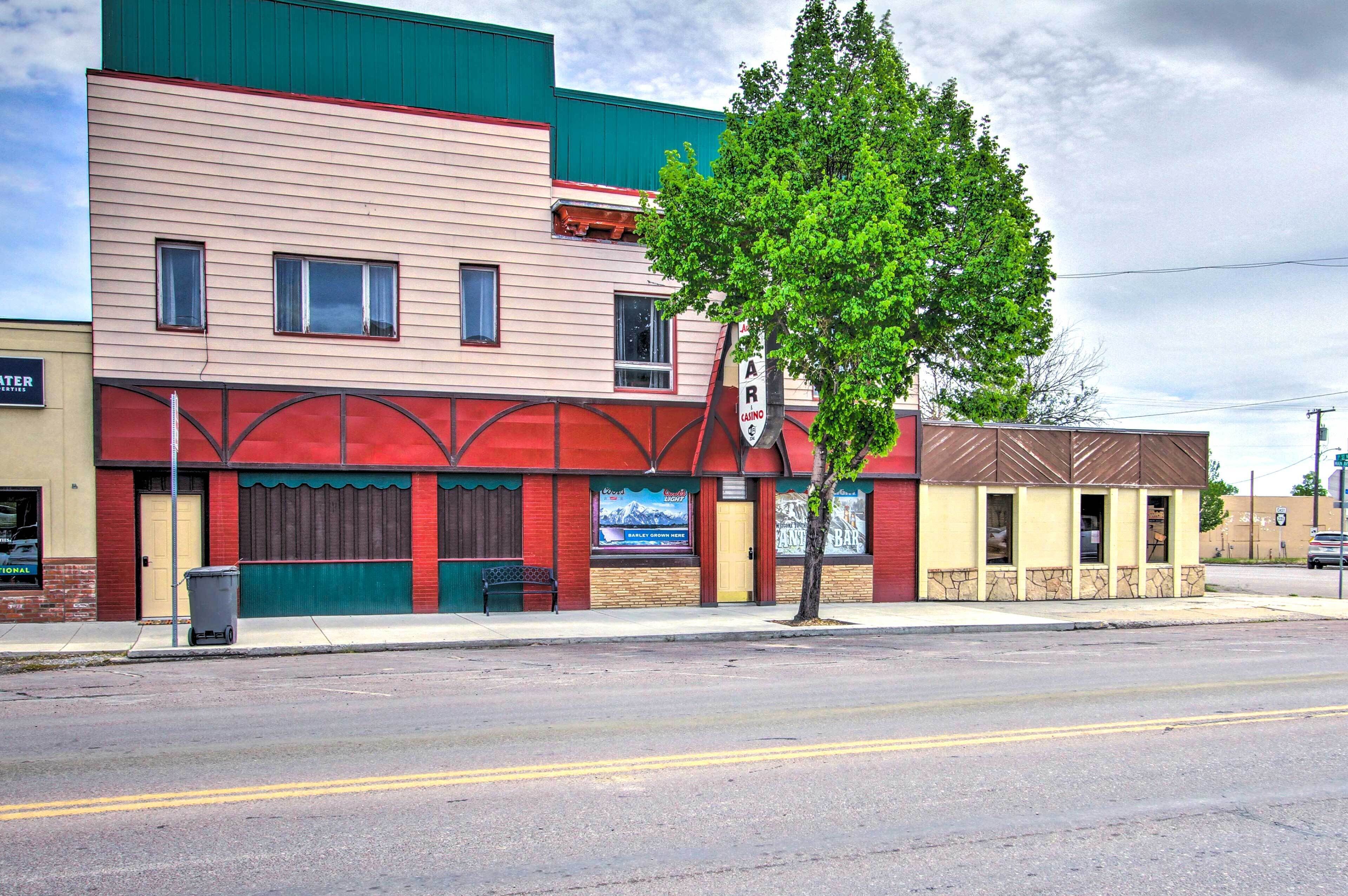A building with a red awning, a sign for a bar, and a tree in front.