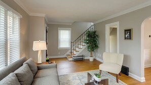 Ein Wohnzimmer mit grauem Sofa, einem weißen Sessel, einem Couchtisch und einer Treppe, die eine weitere Ebene hinaufführt.