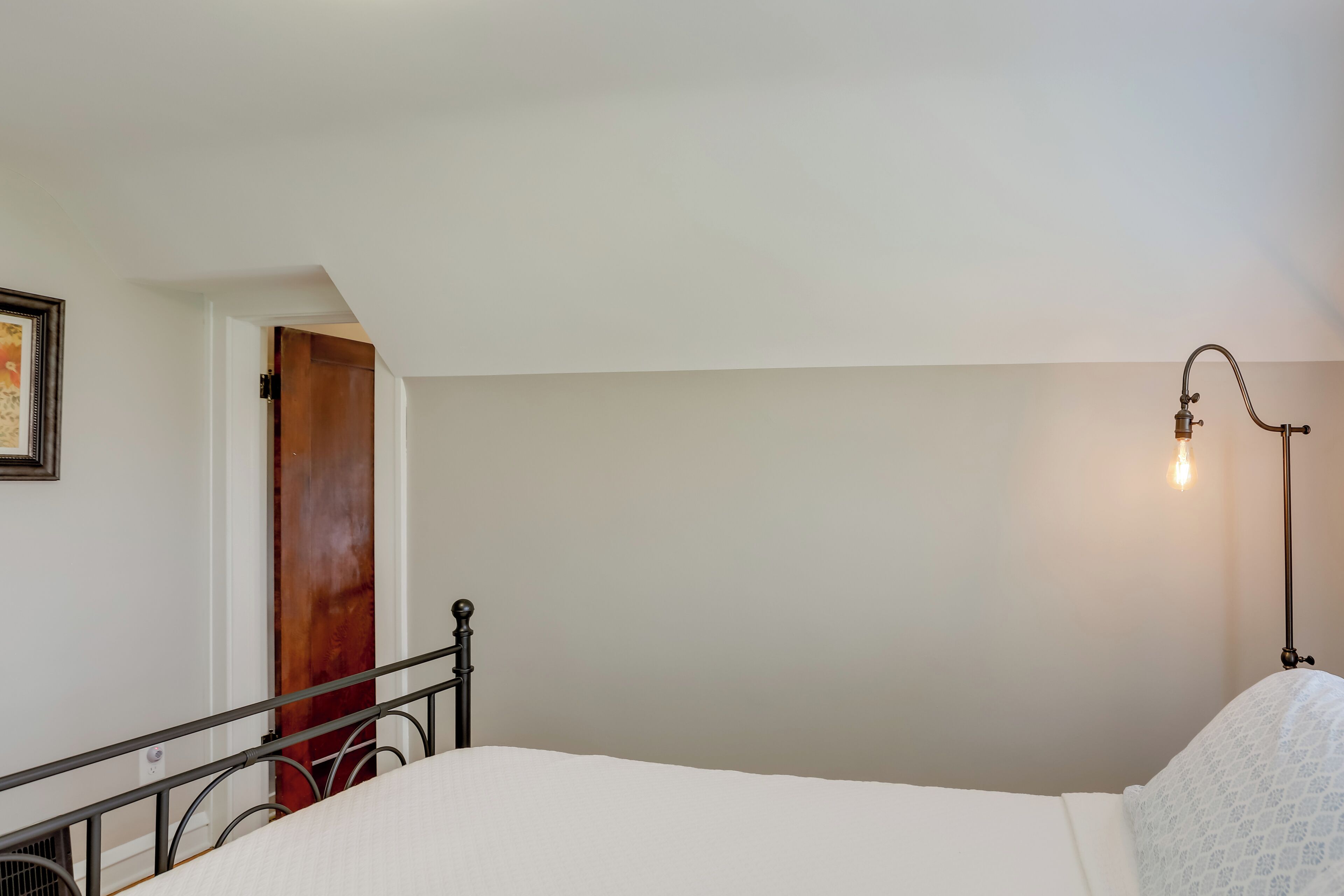 A bedroom with a bed, a nightstand, a lamp, a door, and a framed picture on the wall.