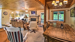 A cozy living room with a fireplace, wooden ceiling, and a dining table. - Robbinsville Cabin w/ Deck: 3 Mi to Fontana Lake! (Robbinsville)