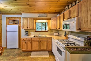 A kitchen with wooden cabinets, a refrigerator, a microwave, a stove, and a sign indicating free lunch tomorrow.