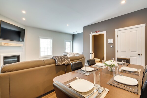 Un comedor con una mesa de madera preparada para cuatro personas, un sofá y un televisor montado en la pared.