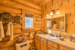 A wooden cabin bathroom with a wooden sink, a large mirror, and a fishing gear sign on the wall. - Cozy Glacier Park Log Cabin - 'best in the West!' (Essex)