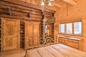 A log cabin bedroom with a bed, wooden cabinets, a dresser, and a stone fireplace. - Cozy Glacier Park Log Cabin - 'best in the West!' (Essex)