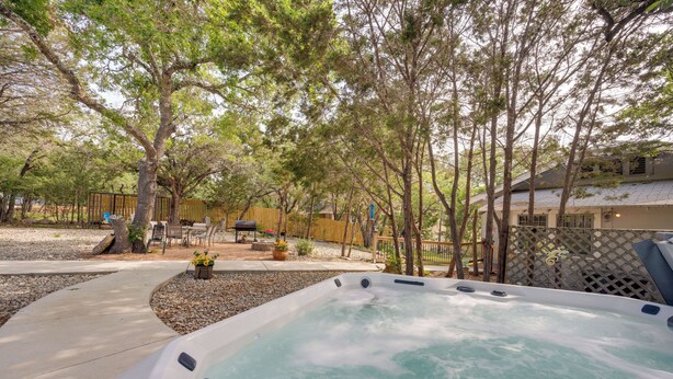 Un bain à remous dans un jardin, avec des arbres, une terrasse et une clôture.