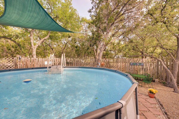 Una piscina cristalina rodeada por una valla de madera, con un letrero que dice "ISLEAR" y una vela de sombra verde por encima.
