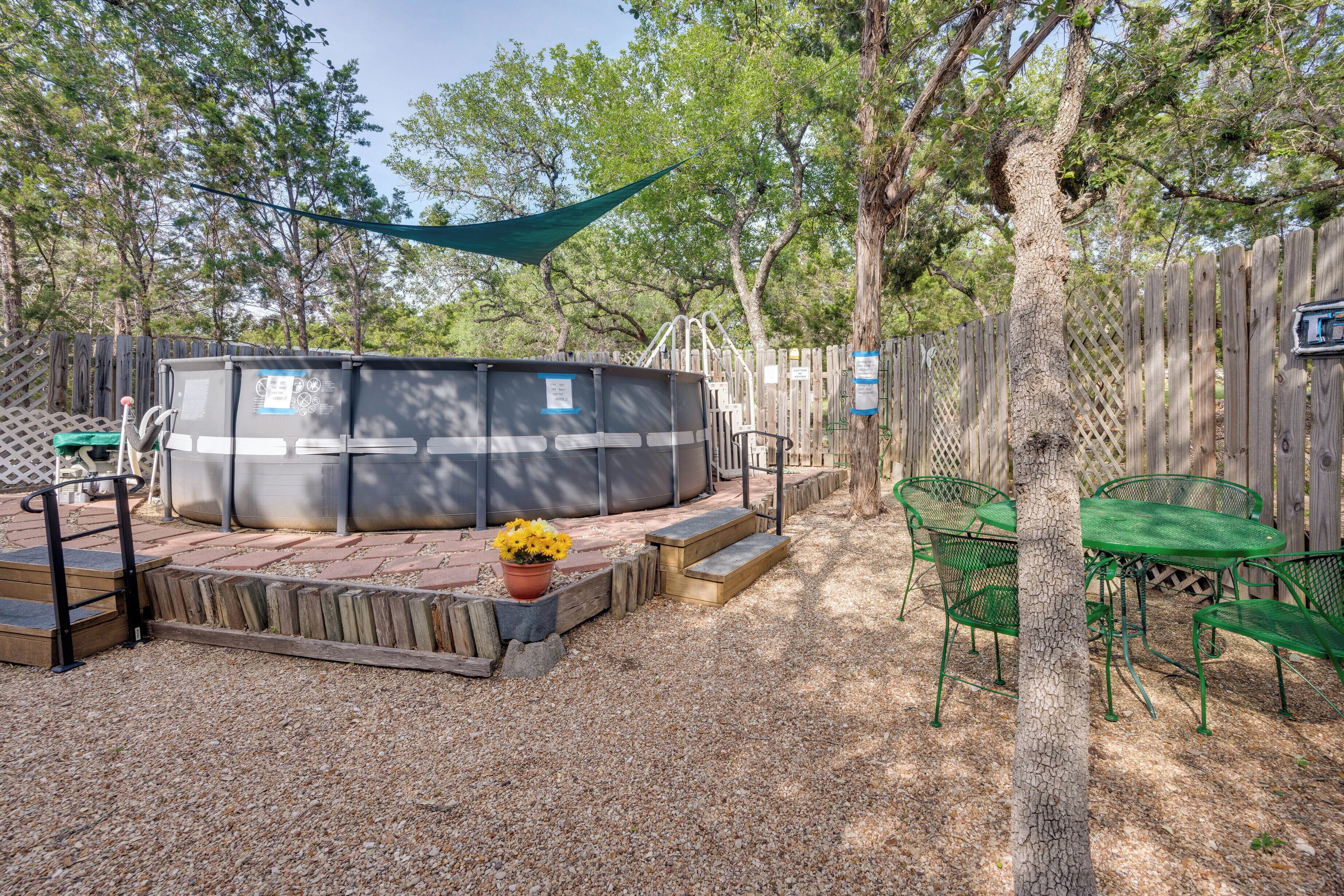 A backyard with a hot tub, a wooden deck, and a fenced area with green metal chairs.