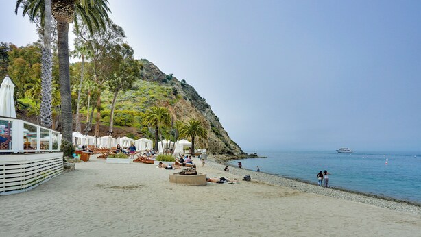 Une plage bordée de palmiers, une colline rocheuse et un bateau sur l’eau.