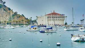 Un port de plaisance où sont amarrés de nombreux bateaux, un grand bâtiment avec un toit rouge et une colline parsemée d’arbres.