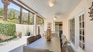 Une terrasse couverte avec une table à manger, des chaises en osier et un vase décoratif.