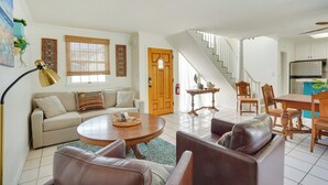 Un salon comprenant un canapé, une table basse et des fauteuils, un coin repas avec une table et des chaises, et une cuisine équipée d’un réfrigérateur.