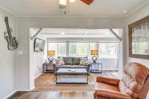 A spacious living room with a sofa, coffee table, and leather armchair. There are two lamps, a guitar, and a framed picture on the wall. - Pet-friendly Somerset Cottage Near Boat Ramps! (Somerset)