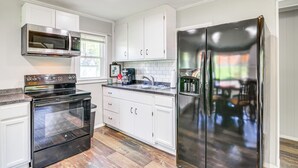 Eine Küche mit weißen Schränken, einem Edelstahlbackofen, einem schwarzen Kühlschrank und einem Fenster über der Spüle.