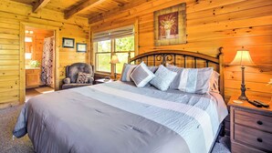 A wooden cabin bedroom with a large bed, a chair, a nightstand, and a window.